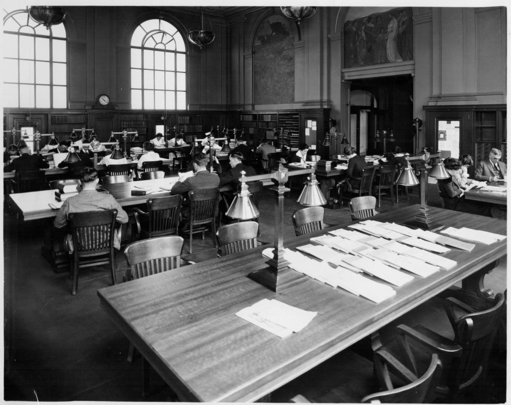 long tables with chairs, some occupied by library patrons studying and reading