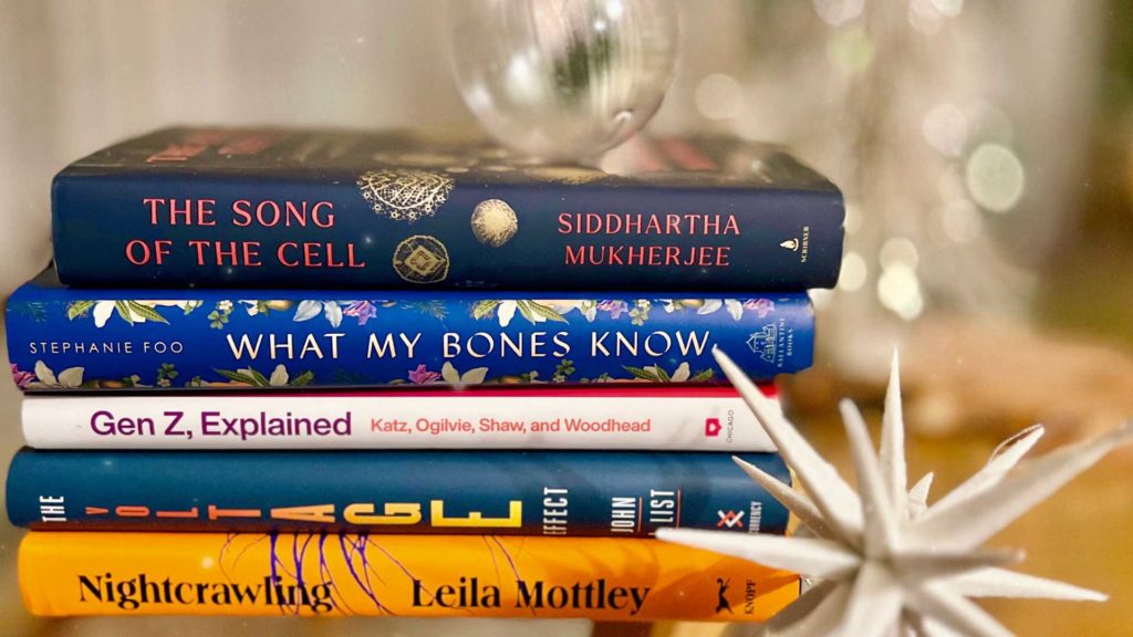 stack of books on Dean's winter reading list with holiday lights in background